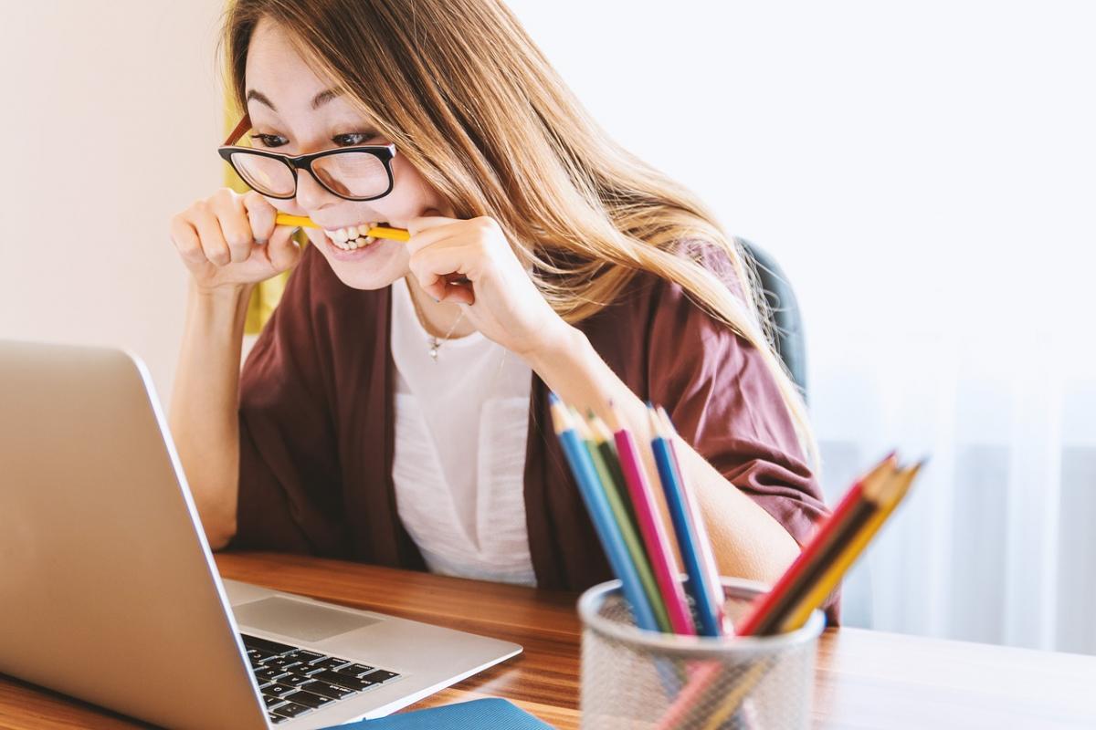 Person biting a pencil in front of a computer.
