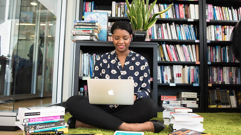 Woman smiling and sitting on the floor with a laptop.