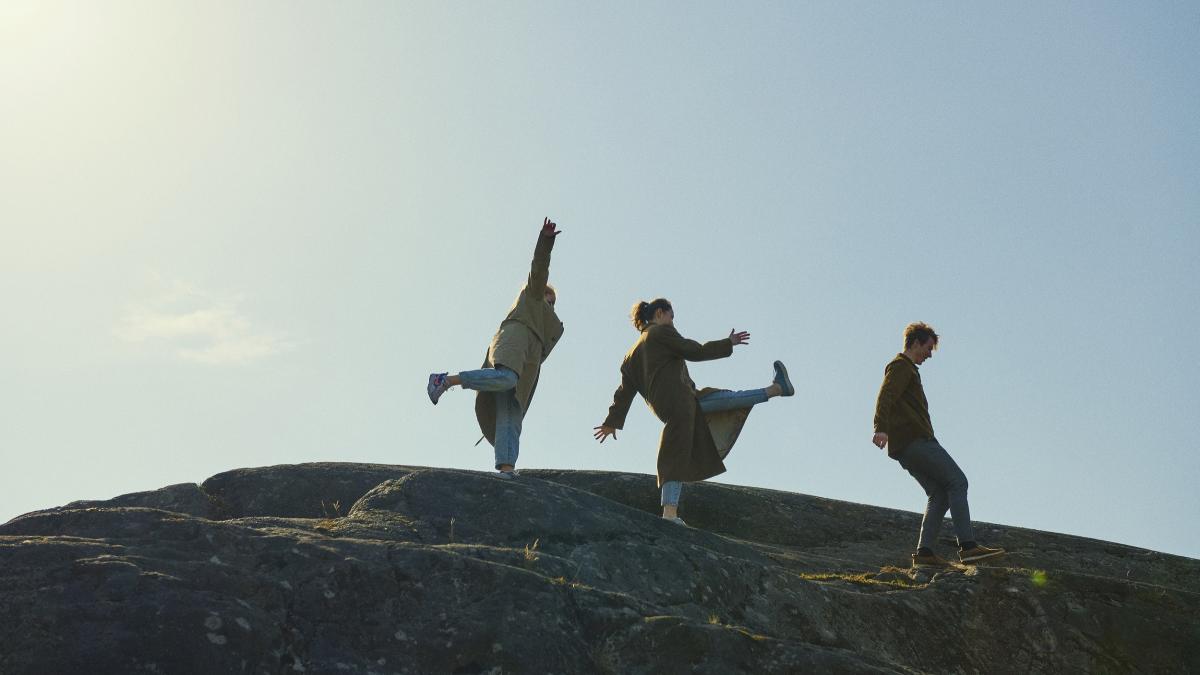 Three people on a rock pictured against the sky.