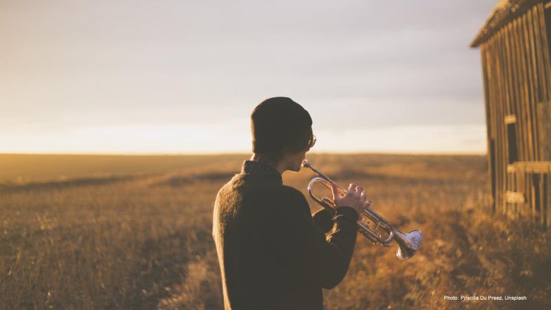 A person plays a trumpet in a field.