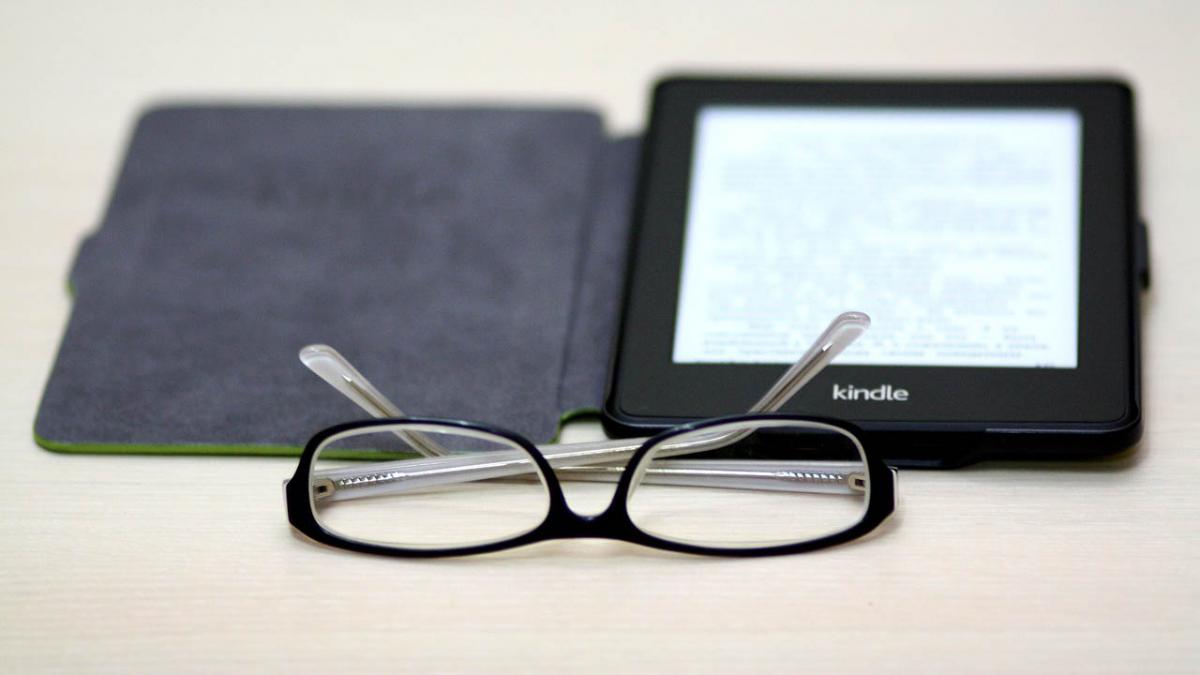 Pair of glasses and a Kindle on a table.