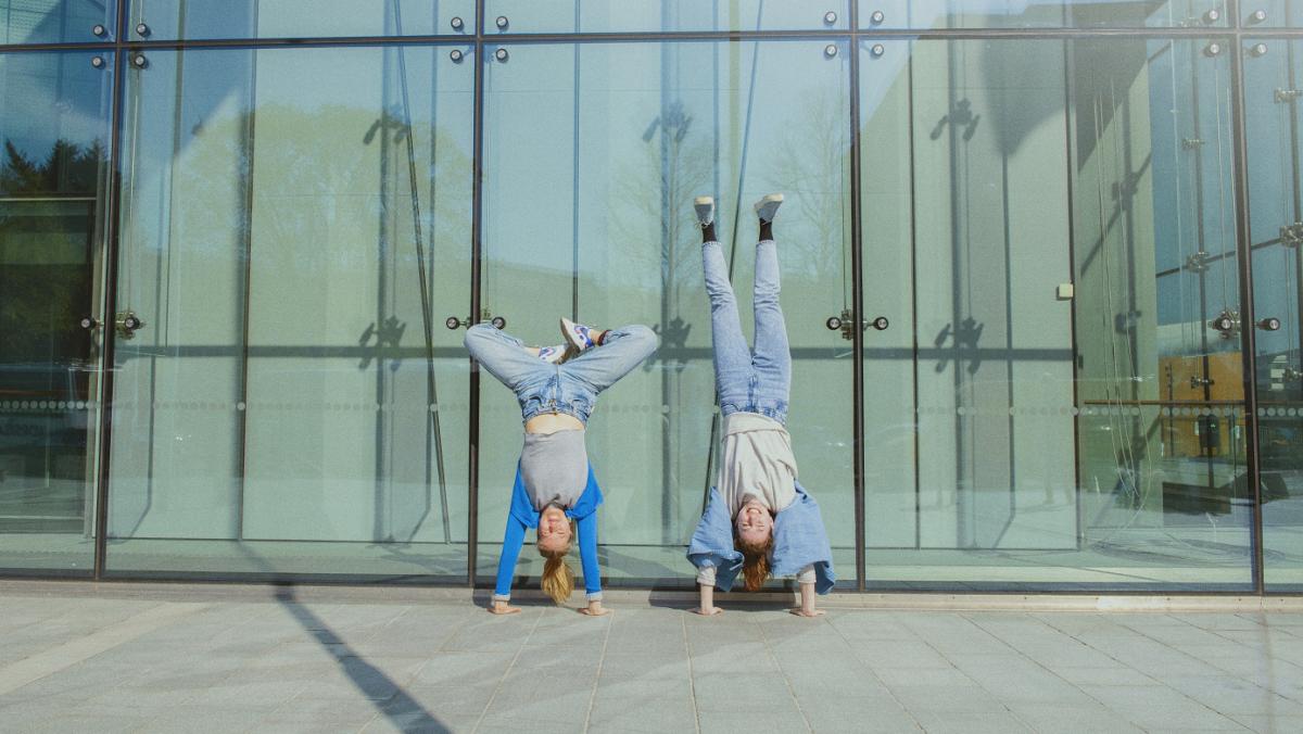 Two persons standing on their hands in front of a building.