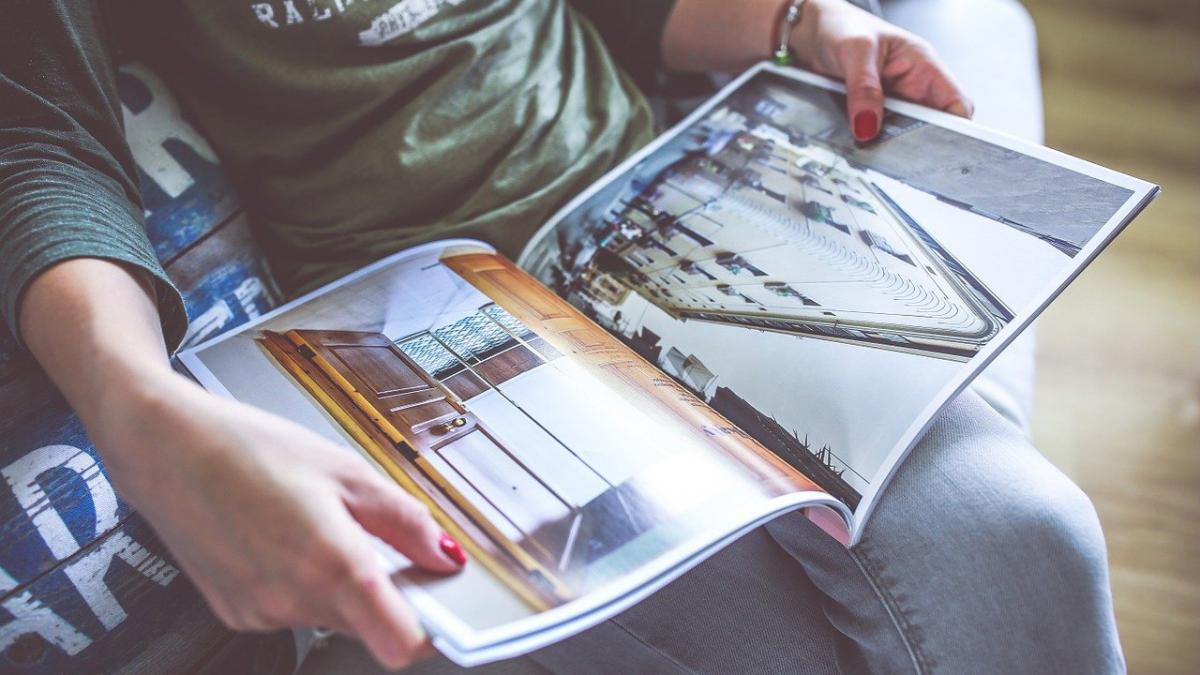 A person reading a magazine on their lap, only hands but not their face can be seen.