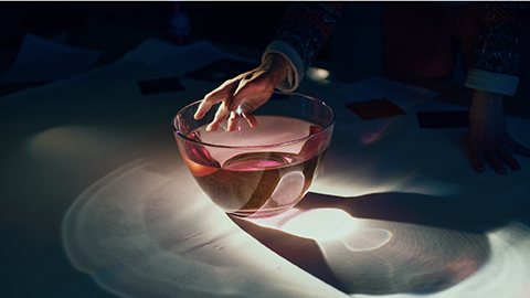 Light red liquid in a transparent bowl and a hand holds on to it.